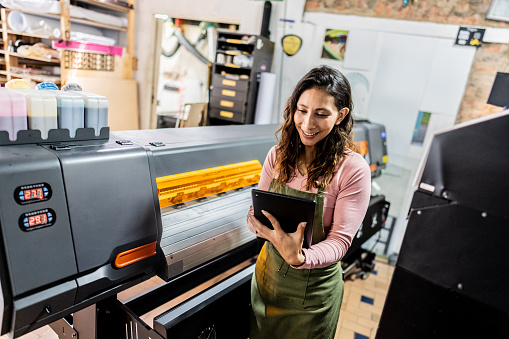 Print shop operator using a tablet beside a printing press